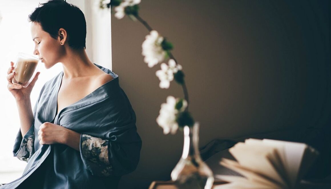 Beautiful woman in blue pajamas having breakfast in bed in morning. Girl drinking coffee.