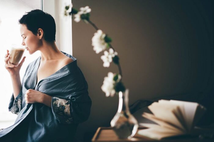 Beautiful woman in blue pajamas having breakfast in bed in morning. Girl drinking coffee.